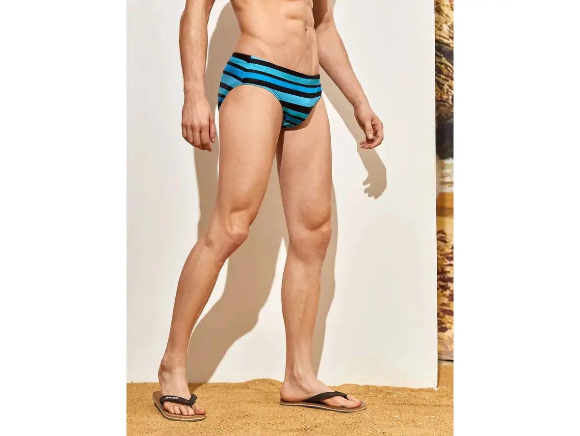 Side profile of black blue stripe swim briefs on sand