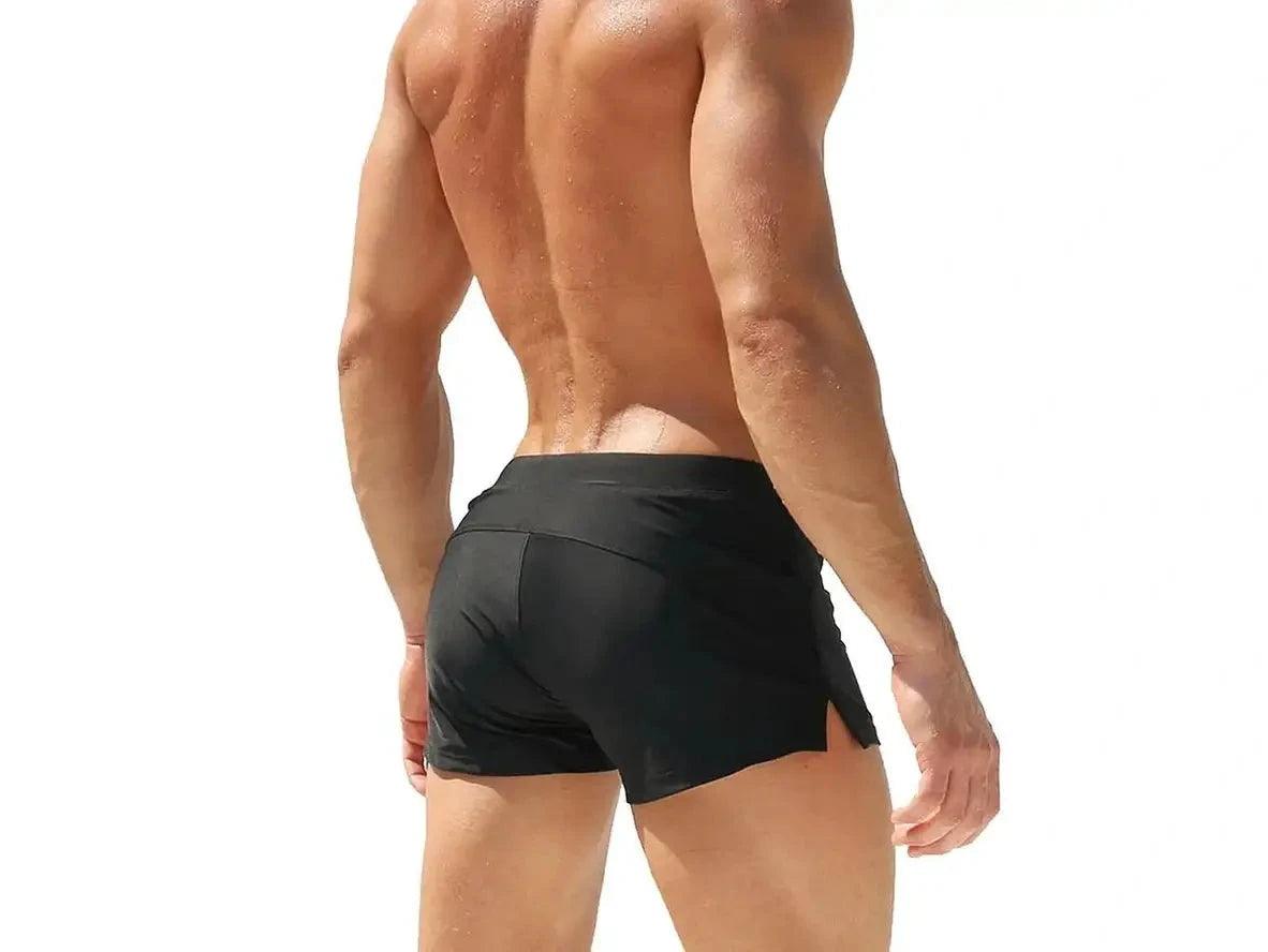 Black low-rise men's swim trunks with water droplets on smooth fabric