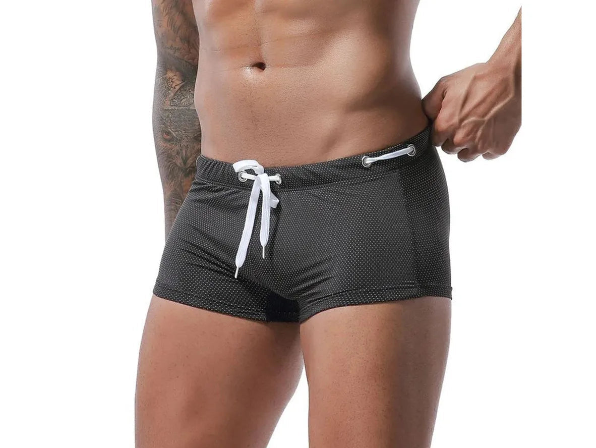 Black low-rise men's swim trunks with white micro-dot pattern and silver eyelets