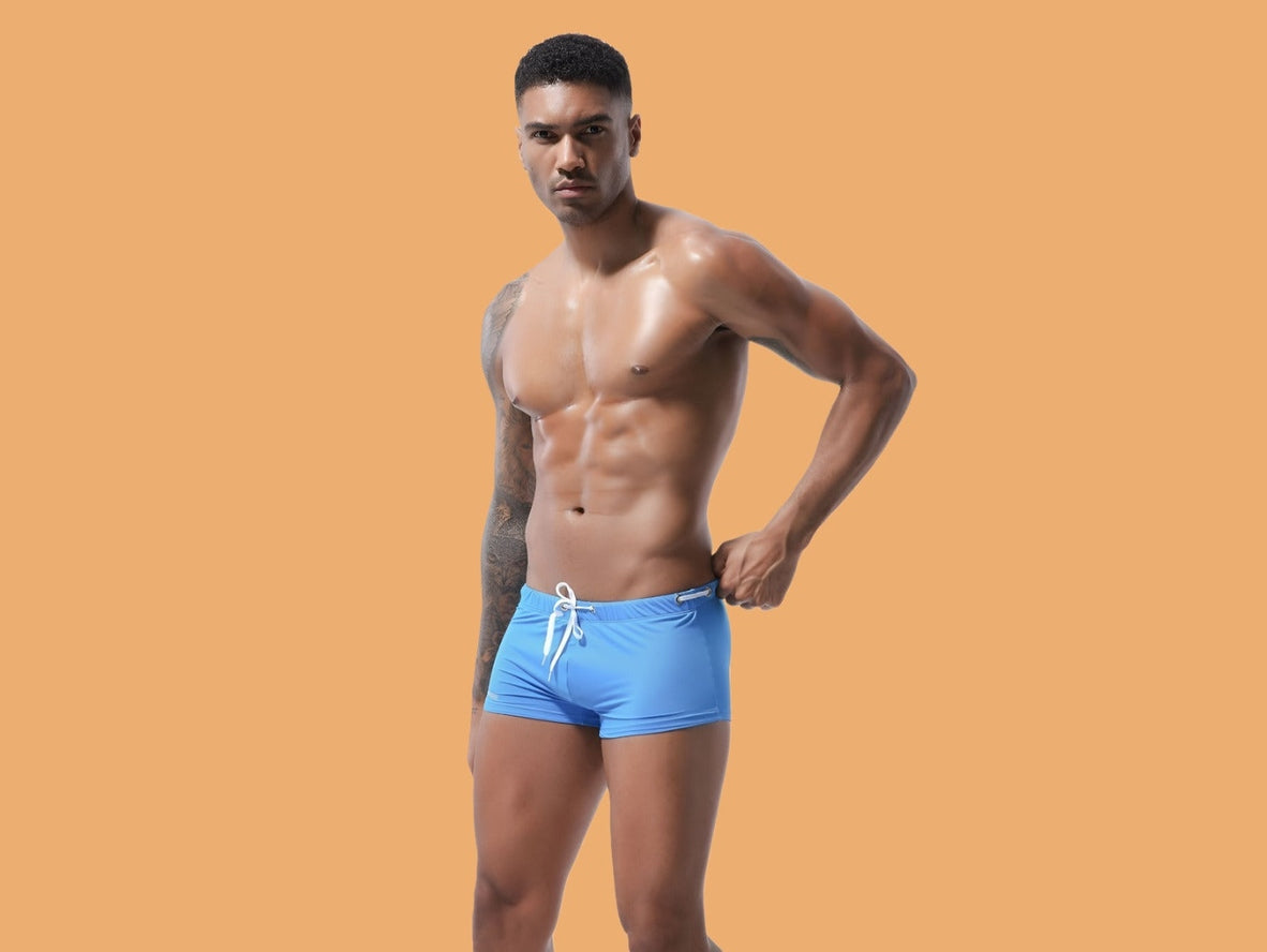 Sky blue low-rise men's swim trunks emphasizing form-fitting cut below navel